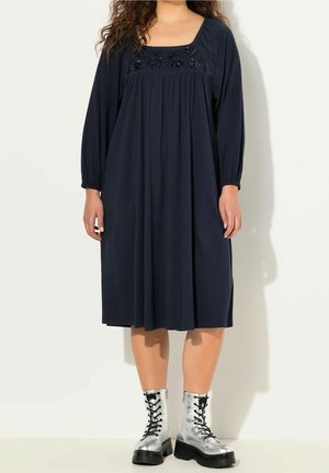 Granatowa sukienka do kolan z długimi rękawami i marszczeniami. Ozdobiona haftowanymi detalami na biuście. Noszona z srebrnymi botkami na sznurowadła.