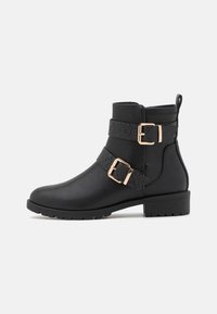 Botas negras hasta el tobillo de cuero sintético que presentan dos correas texturizadas con hebillas doradas, una puntera redondeada y un tacón bajo de bloque.