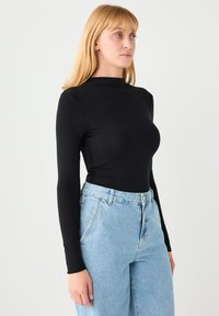 Czarna bluzka z długim rękawem wykonana z elastycznego materiału, z wysokim dekoltem. Połączona z luźnymi jasnoniebieskimi jeansami o klasycznym fasonie z pięcioma kieszeniami.