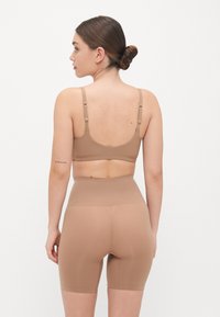 Brown seamless sports bra and high-waisted shorts. Made from stretchy fabric with a smooth texture, featuring adjustable straps and a minimalist design.