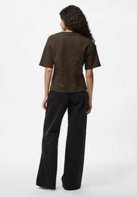 Brūns īsām piedurknēm T-krekls, kas saskaņots ar brīvām melnām biksēm. Audums izskatās mīksts, ar brīvu piegriezumu un minimālu detaļu skaitu.