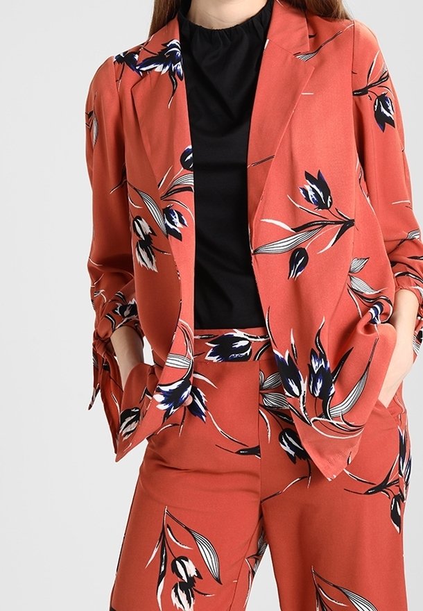 Rudí oblek s květinovým vzorem v modré a bílé barvě, vyrobený z hladkého materiálu, s upraveným blejzrem a volnějšími kalhotami.