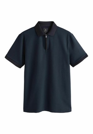 Lyhythihainen polo-paita tummansinisessä värissä, jossa on hienovarainen timanttimäinen kuvio, vetoketjullinen kaulus sekä mustat kontrastisomisteet hihoissa ja kauluksessa.