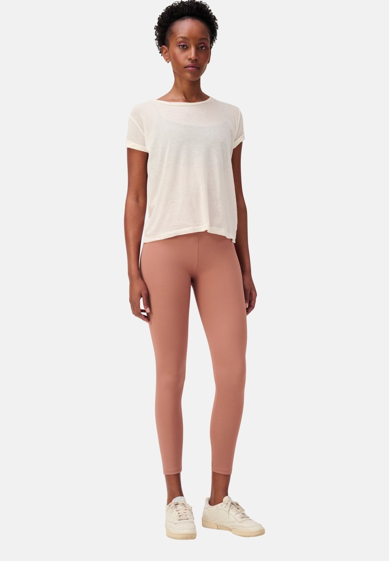 T-shirt beige chiaro a maniche corte, leggings pesco aderenti e sneakers bianche, con una superficie liscia e un design minimalista.