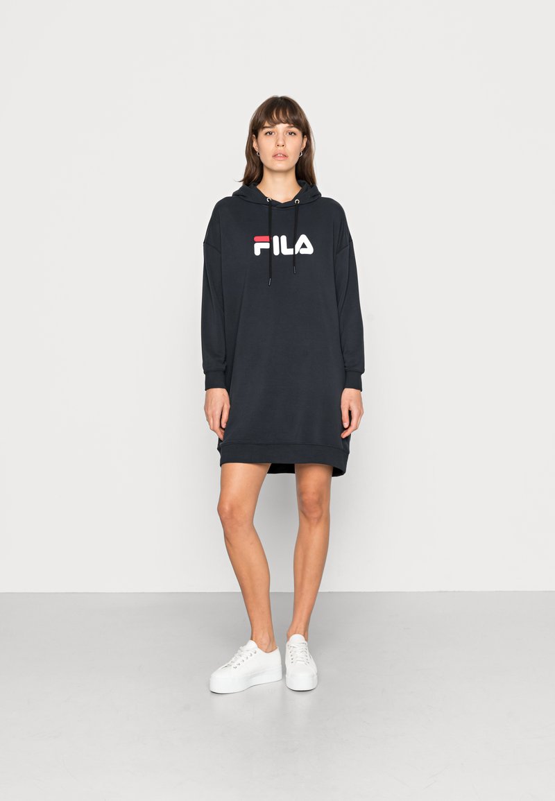 Vestito felpa nero con cappuccio e logo Fila in bianco e rosso. Tessuto morbido, maniche lunghe, vestibilità comoda e tasche laterali. Indossato con sneaker bianche.