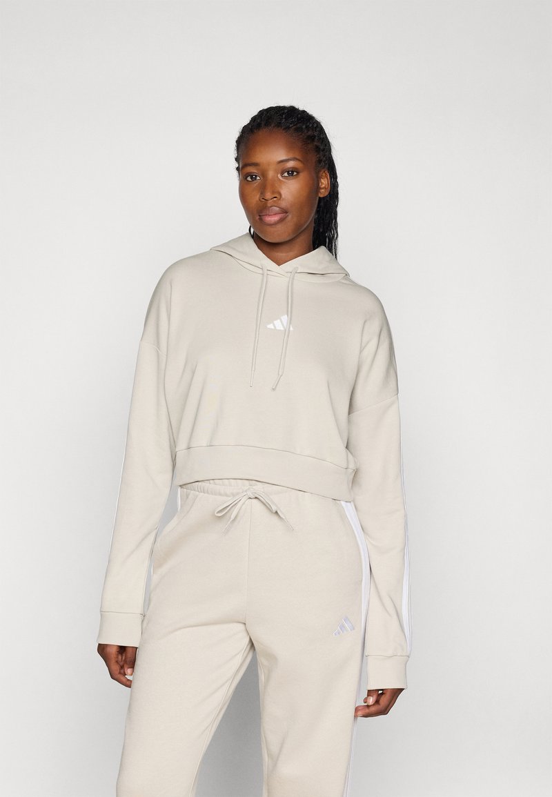Lichtbeige cropped hoodie met een voorzak en wit logo, gecombineerd met bijpassende joggers met zijstrepen en een verstelbare tailleband.