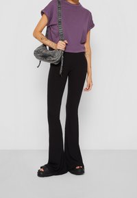 Lila kortärmad t-shirt, ribbade svarta utsvängda byxor och svarta plattformssandaler. Grå axelväska med tygrem och dragkedjedetalj.