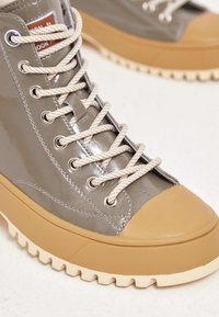 Wysokie trampki z błyszczącą szarą cholewką, beżowym gumowym noskiem oraz kremową, teksturowaną podeszwą, grubymi sznurowadłami i metalowymi oczkami.