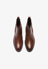 Botas de cuero marrón hasta el tobillo con paneles laterales elásticos, punta redondeada y lengüetas. Textura suave y detalles de costura mínimos.