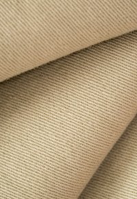 Primer plano de una tela de sarga beige que muestra una textura acanalada diagonal y fibras suaves tejidas.