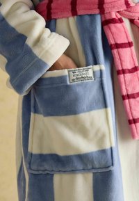 Pehme päevitusriie, millel on sinised ja valged triibud, roosade ruudustikku kuuluv vöö ning taskul silt "JOULES HIBERNATE".