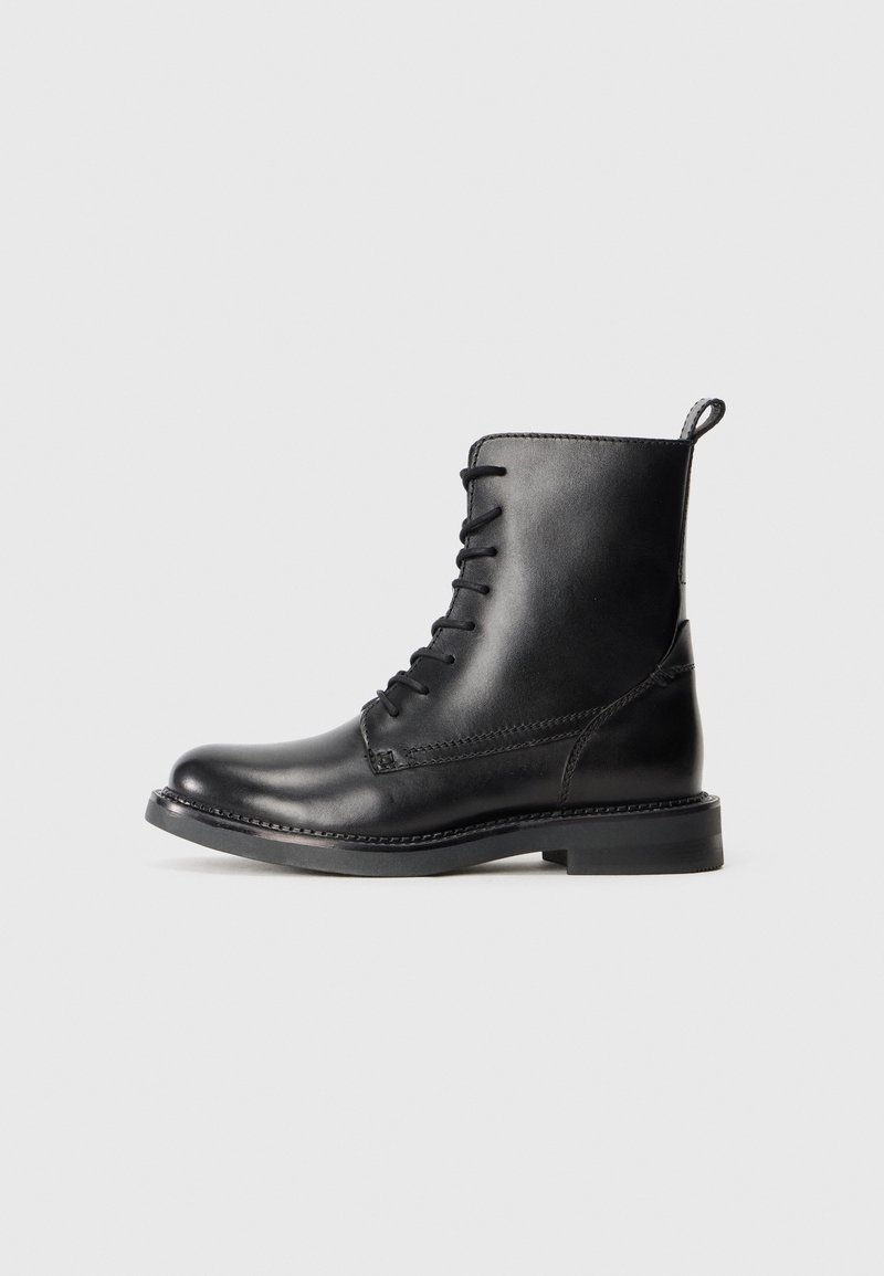 Bottine noire en cuir à lacets avec languette, bout arrondi et petit talon bloc sur un fond gris clair.