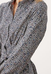 Camicia abbottonata in tessuto blu scuro con un piccolo motivo di cuori multicolori. Maniche lunghe con una silhouette aderente e colletto.
