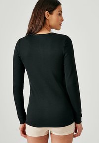 Top a maniche lunghe nero a coste con scollatura rotonda e silhouette aderente, che mette in risalto una texture liscia e una lunghezza delle maniche estesa.