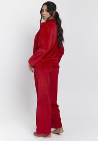 Red velour loungewear set featuring a long-sleeve top and wide-leg pants, with a soft texture and ribbed pattern.