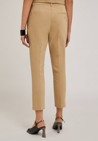 Pantaloni beige su misura con una texture liscia, dotati di due tasche posteriori e un design a gamba dritta e corta. Abbinate a tacchi neri e argento.