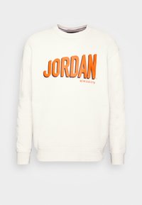 Sweatshirt crème avec lettrage orange "JORDAN". Il possède un col rond, des manches longues ainsi que des poignets et un ourlet côtelés. Texture lisse.
