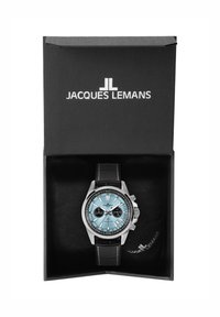 Jacques Lemans laikrodis juodame dėžutėje. Jame yra sidabrinė korpusas, turkio spalvos ciferblatas, juodi subciferblatai ir juodas odinis dirželis.