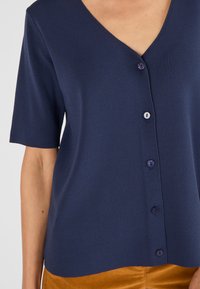 Top de punto de manga corta en azul marino con escote en V y cinco botones, con tejido texturizado y acentos de botones morados.