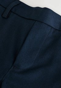 Navyblaue Stoff mit leichtem Schimmer, verfügt über eine flache Vorderseite, ein Taillenband und genähte Details. Geschmeidige Textur mit einem dezenten Webmuster.