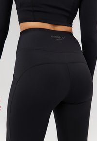 Leggings de sport noirs avec une taille haute, présentant un design texturé et des coutures plates. Marque visible sur la taille.