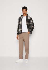 Melnā un baltā pleda žakete virs baltas T-krekla, bēšas bikses un baltas sporta kurpes. Žaketē ir pogāta priekšpuse un divas kabatas.