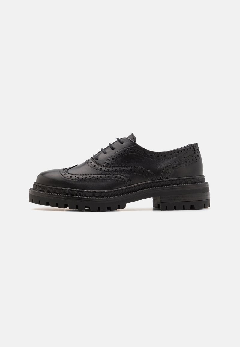 Chaussure brogue en cuir noir avec détails à bout ailé, devant à lacets et semelle épaisse et robuste, vue de profil sur fond blanc.