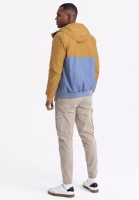 Hoodiejacka med en design i gult och blått, elastisk midja, buren med beiga cargobyxor och vita sneakers. Synliga sömdetaljer.