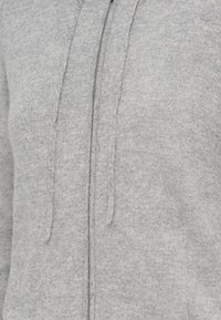 Sweatshirt cinzento feito de tecido suave, com fecho éclair à frente, capuz com cordão e acabamento texturizado. Detalhes de costura visíveis ao longo das costuras.