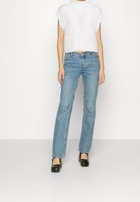 Bílý pletený krátký top s vysokým výstřihem, ve spojení se světle modrými džíny s rovnými nohavicemi a černými platformovými botami.