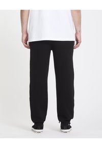 Pantalons de survêtement noirs avec une taille élastique et des poignets, fabriqués en tissu doux. Portés avec des baskets noires avec une semelle blanche.