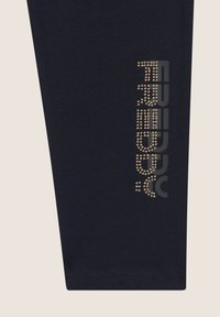 Leggings blu navy realizzati in tessuto elasticizzato, con un logo borchiato in argento e oro sul lato e una texture liscia in tutta la superficie.