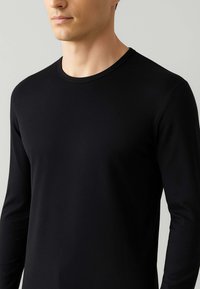 Maglietta nera a maniche lunghe con collo rotondo. Realizzata in un tessuto morbido e liscio, con un taglio aderente e cuciture minime, che enfatizzano un design elegante.