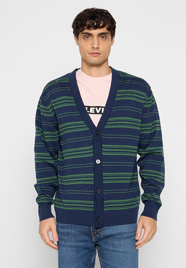 Marineblauwe cardigan met groene horizontale strepen, v-hals, lange mouwen en een sluiting met vijf knopen. De stof lijkt gebreid met ribbelmanchetten.