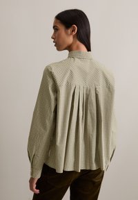 Groen en wit geblokt shirt met een hoge kraag, geplooide achterkant en knoopmanchetten. Gemaakt van stof met een gladde textuur.