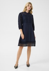 Navy blue dress with lace bodice, three-quarter length sleeves, and button closure. Detailed lace hem with scalloped edges.