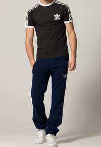 Svart bomulls-t-shirt med vita detaljer och logotyp; marinblå fleecemjukisbyxor med elastisk midja; vita sneakers. Atletisk passform och avslappnad stil.