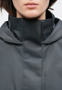 Siva jakna s kapuco, ki ima visok ovratnik in gladko teksturo. Tkanina ima rahlo sijajnost in diagonalne rebraste vzorce.