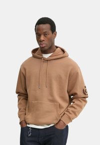 Felpa marrone con cappuccio e coulisse, tasca frontale e logo sul maniche. Realizzata in tessuto morbido con una trama liscia.
