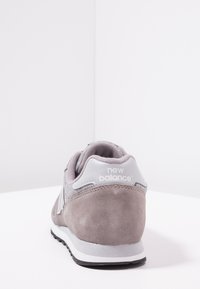 Szare zamszowe sneakersy z textured tylną częścią, wyściełanym kołnierzem i białymi akcentami. Z logo "New Balance" na pięcie.