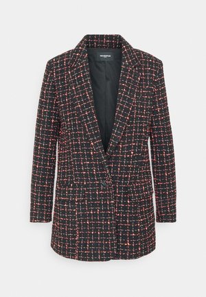 Henkilö, joka pukeutunut mustiin liehuviin housuihin, punamustaan ruudulliseen bleiseriin, mustaan toppiin ja mustiin korkokenkiin, pitäen mustaa kultaketjulla varustettua clutch-laukkua.