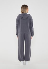 Felpa grigia con tasca a marsupio e pantaloni larghi abbinati. Realizzata in tessuto morbido, presenta un cappuccio regolabile. Sneakers bianche completano il look.