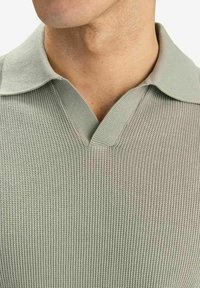 Ljusgrön texturerad stickad tröja med V-ringning och klassisk krage. Nära vy framhäver vävningen och kragsdetaljerna.