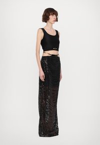 Black crop tank top with wide straps and a decorative gold clasp, paired with a floor-length black sequin skirt featuring wave patterns.