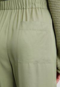 Light green pants featuring a waistband with elastic and a large patch pocket on the back, made from a smooth, lightweight fabric.