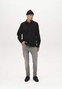 Must mustaga särk kahe rinnataskuga, hall slim-fit teksad ja mustad kingad. Mudel kannab musta kudumist beanie'i. Lihtne taust.