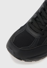 Black athletic shoe with a mesh upper, textured leather accents, and round laces. Curved rubber sole with a slight tread pattern.