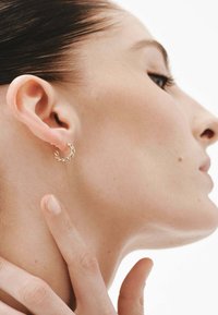 Pendiente de aro de oro con un diseño retorcido, llevado en la oreja. Textura suave, tamaño pequeño, que muestra una apariencia delicada e intrincada.