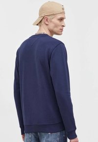 Felpa blu navy con maniche lunghe, polsini e orlo a coste, cucitura a V sul retro, realizzata in un tessuto morbido e testurizzato.