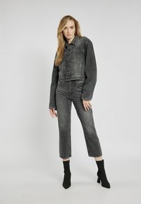 Czarna kurtka dżinsowa o kroju cropped, zestawiona z szarymi, wysokim stanem dżinsami w delikatny, cętkowany wzór. Wysokie czarne botki na obcasie.